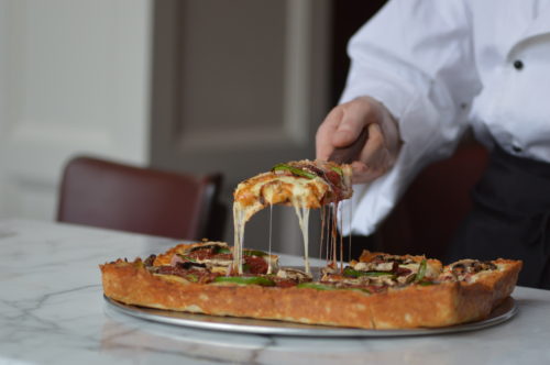 A square slice of Shield's deep-dish pizza being lifted, cheese stretching