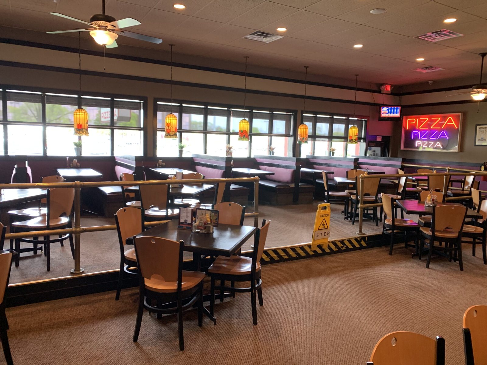 Shield's dining room with red booths, pendant lamps and a neon pizza sign